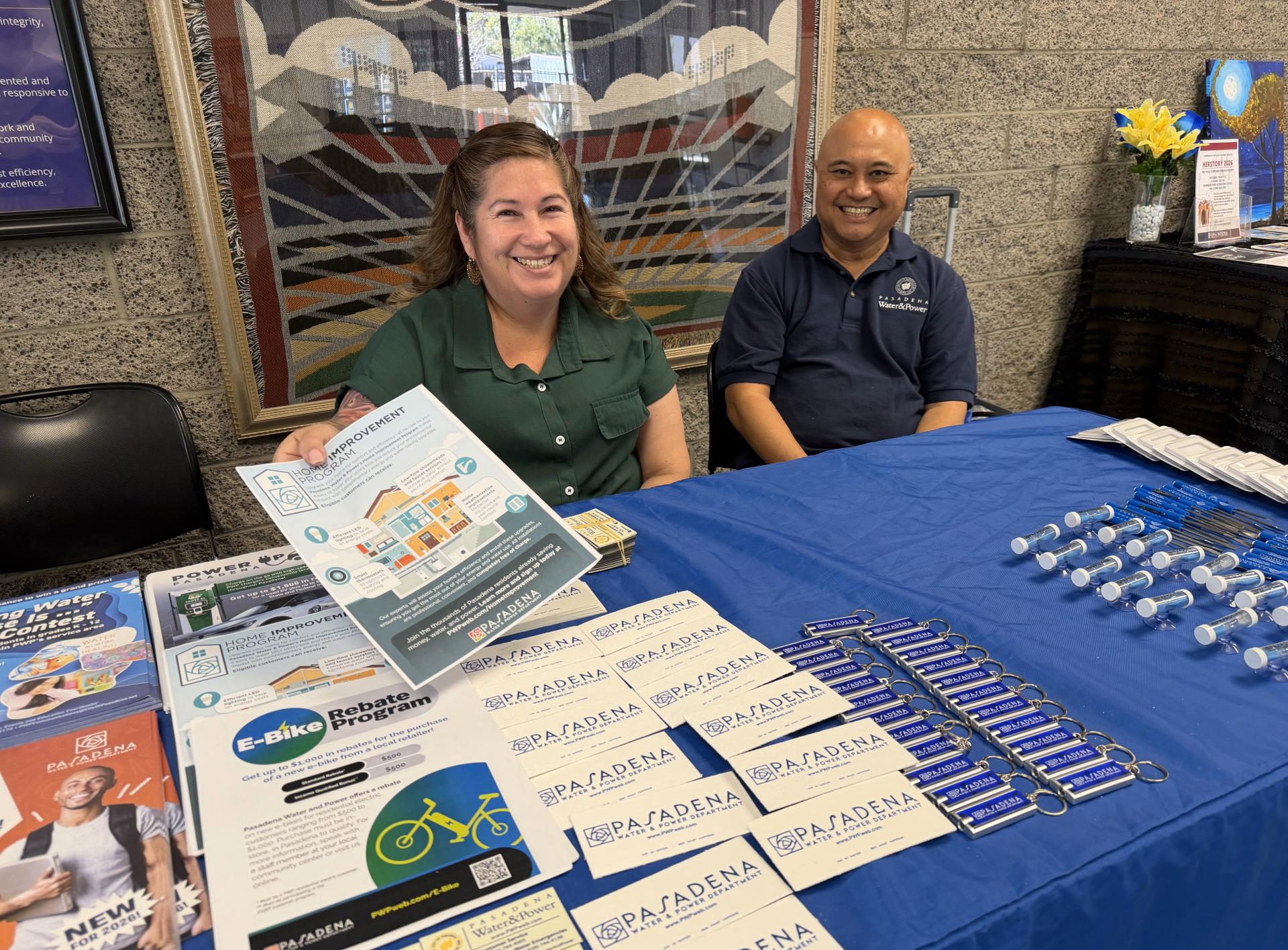 Two Pasadena Water and Power sit at an informational booth table handing out flyers.
